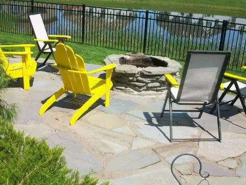 A flagstone patio with a fire pit and yellow chairs