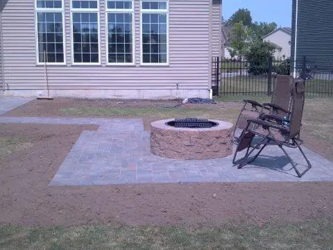 A paver patio with a round fire pit in a back yard
