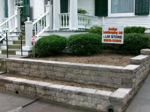 Block retaining walls along a front walk, with an LM Stone yard sign