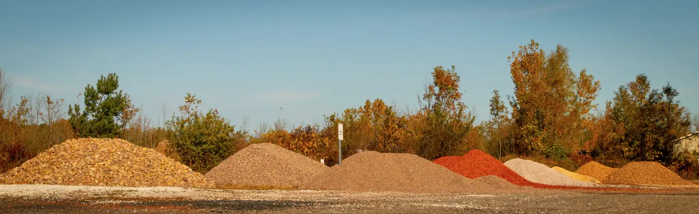 A row of bulk stone piles in the yard: tan, grey, red and white stone
